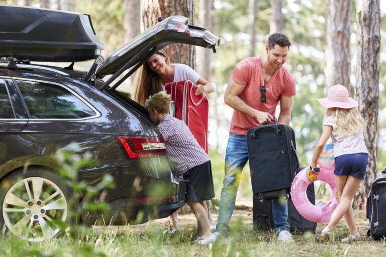Kinder helfen Eltern beim Gepäcktragen zum Auto vor der Reise in den Urlaub.